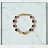 Gold bracelet with red and blue gemstones on a marble surface