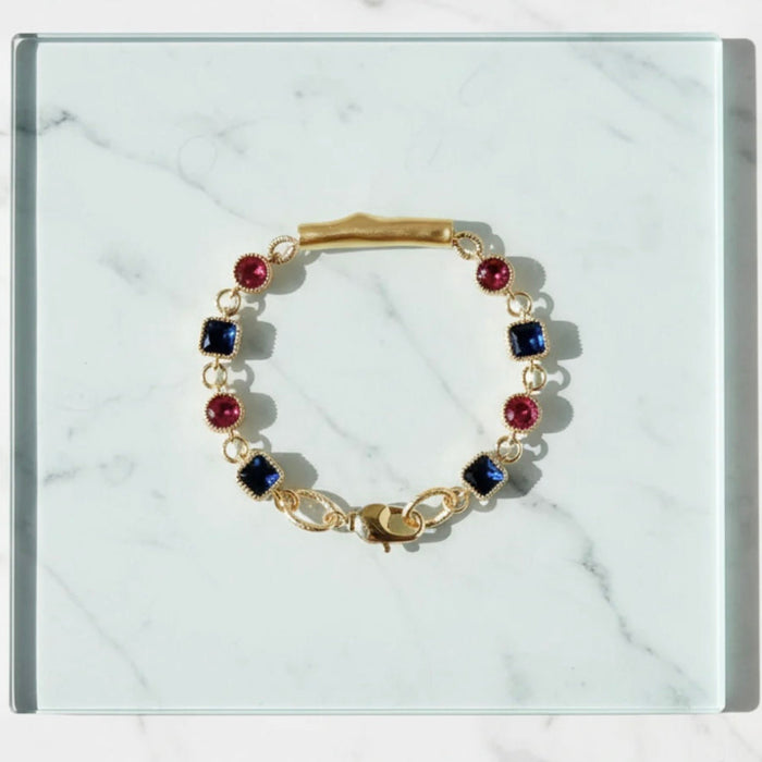 Gold bracelet with red and blue gemstones on a marble surface