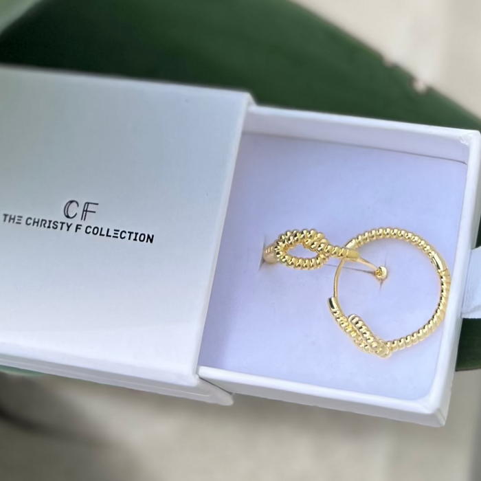 Gold earrings in a white box with 'CF' branding on a green leaf background