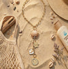 Necklace with shell and pearl charms on sand with beach accessories