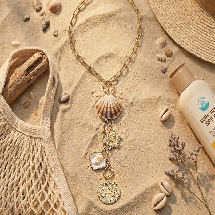Necklace with shell and pearl charms on sand with beach accessories