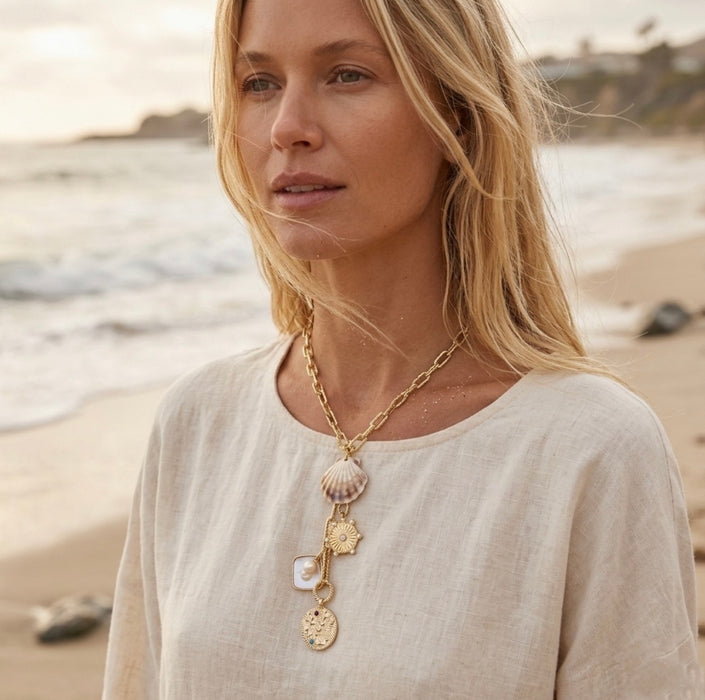Woman on a beach wearing a gold necklace with various pendants.