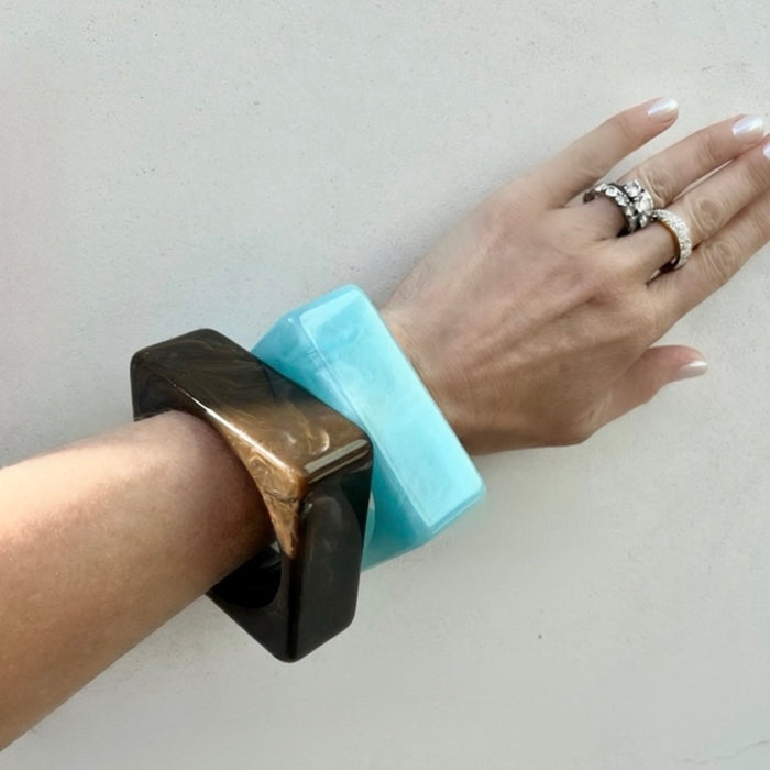 Hand wearing a turquoise bracelet with a black square clasp on a light background