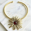 Gold necklace with a starburst design and red gemstone on a marble surface