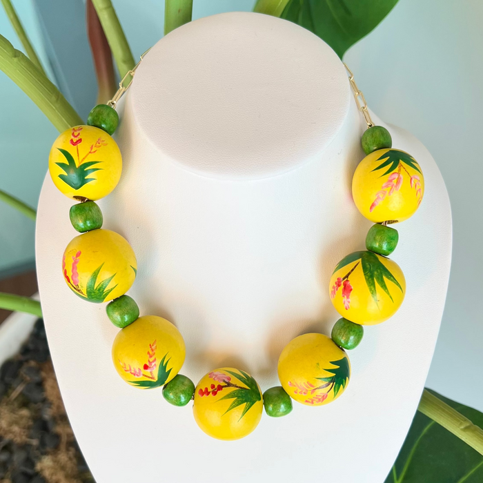 Necklace with yellow and green beads on a mannequin bust against a natural background.