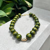 Green beaded necklace with gold clasp on a gray surface with greenery in the background