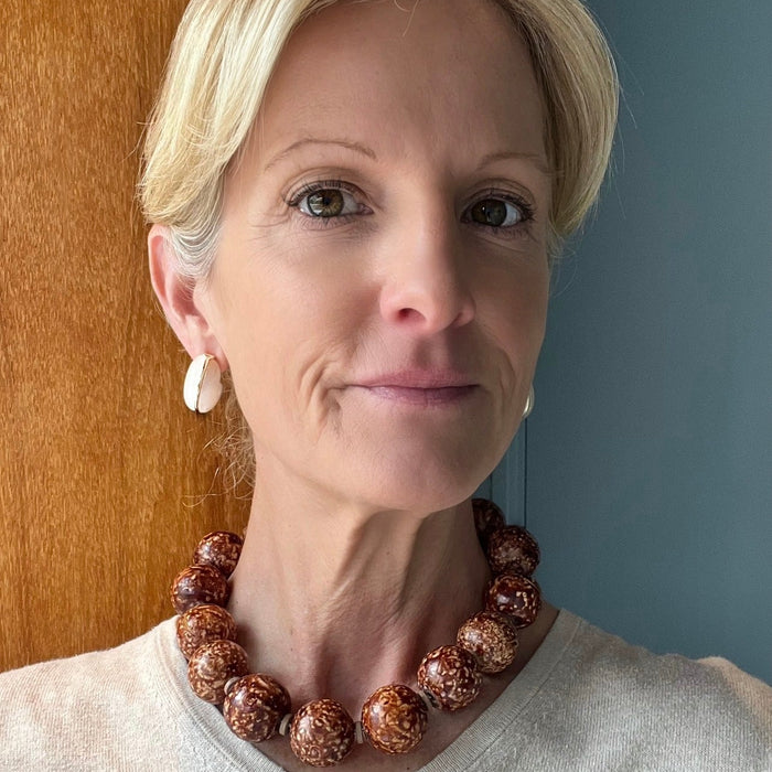 Woman wearing a brown beaded necklace against a neutral background