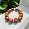 Brown beaded bracelet on a textured surface with green leaves in the background