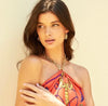 Woman wearing a colorful dress with a gold necklace against a beige background