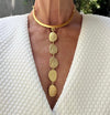 Gold necklace with circular pendants worn by a person against a white textured garment.