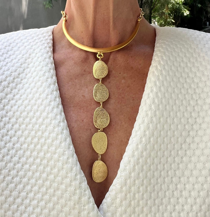 Gold necklace with circular pendants worn by a person against a white textured garment.