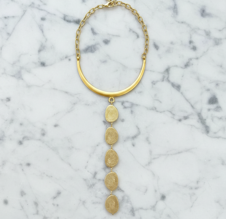 Gold necklace with circular pendants on a marble surface