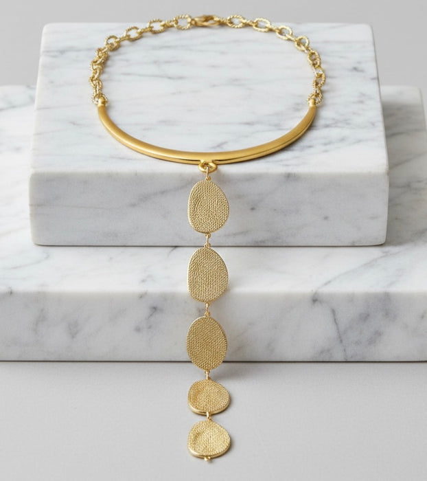Gold necklace with circular pendants on a marble surface