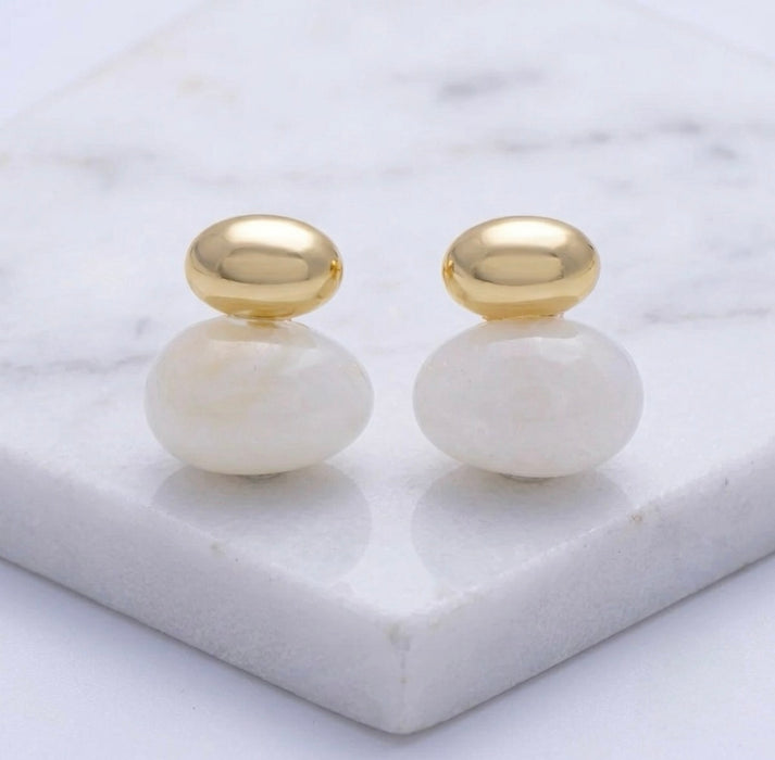 Pair of gold and white earrings on a marble surface