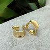 Gold hoop earrings on a textured surface with green leaves in the background