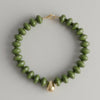 Green beaded bracelet with a gold clasp on a marble surface