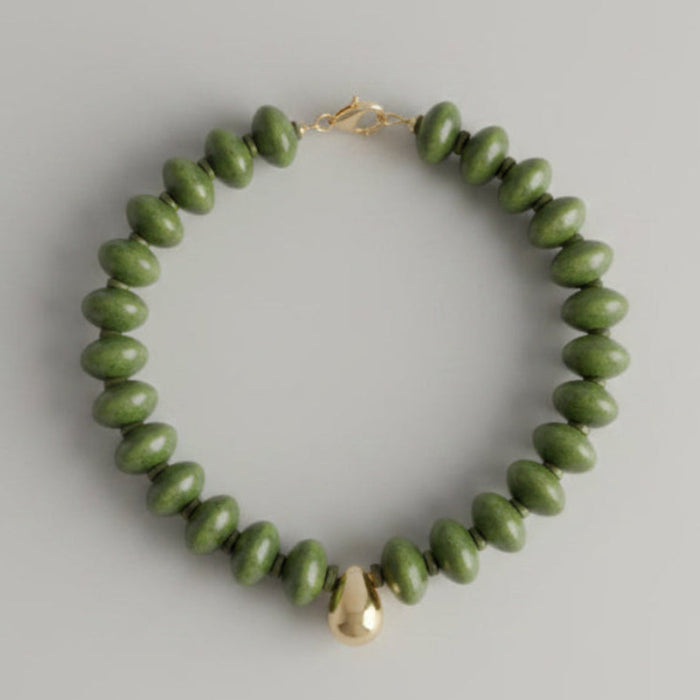 Green beaded bracelet with a gold clasp on a marble surface
