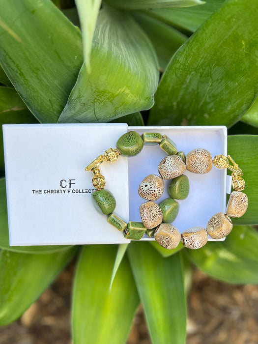 Two beaded bracelets on a white card with 'CF' branding, set against a green leafy background.