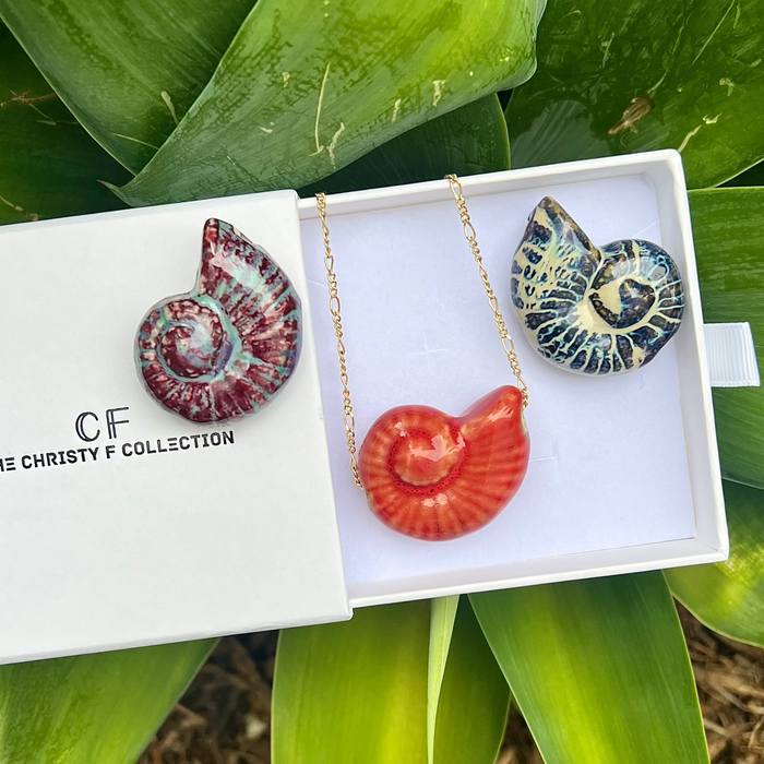 Jewelry set in a box with 'CF' branding, surrounded by green leaves.