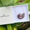 Necklace with a shell pendant in a white box labeled 'CF Collection' on green leaves.