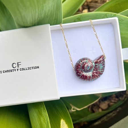 Necklace with a shell pendant in a white box labeled 'CF Collection' on green leaves.