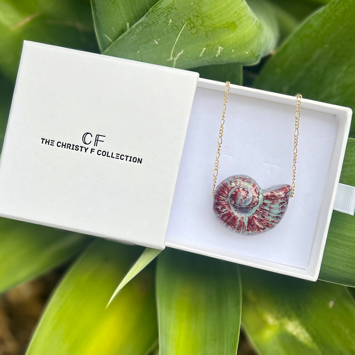 Necklace with a shell pendant in a 'CF The Christy F Collection' box against a green leafy background