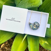 Necklace with a decorative pendant in a 'The Christy F Collection' box on green leaves.