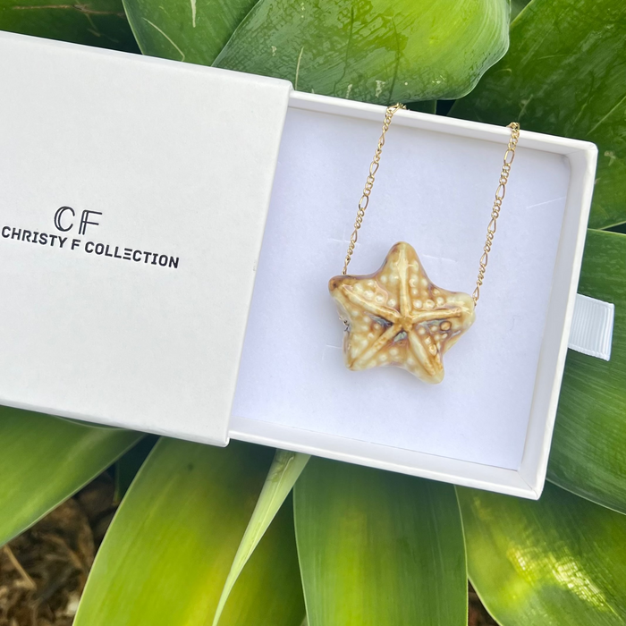 Gold starfish necklace in a Christy F Collection box with green leaves in the background