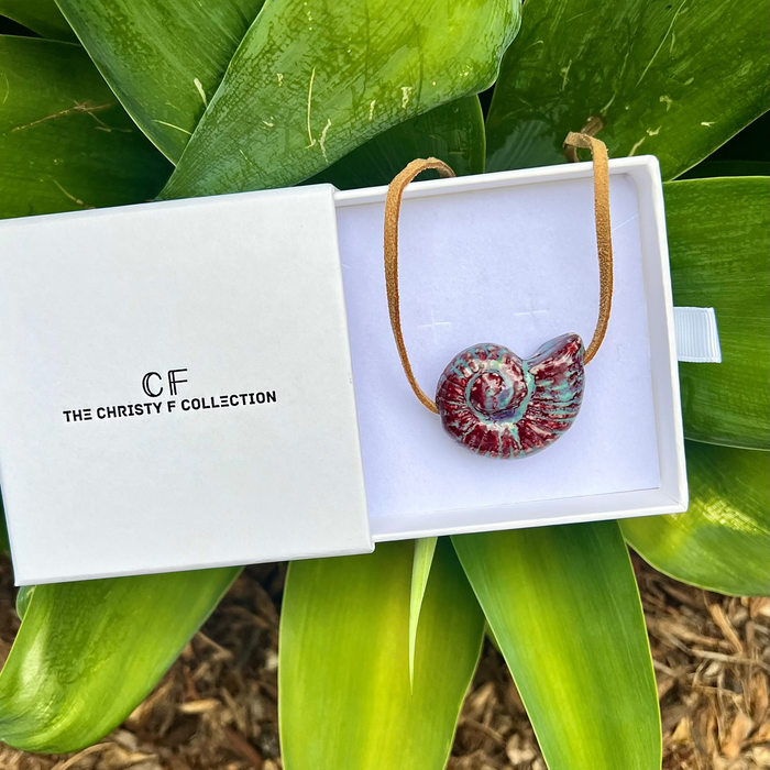 Necklace in a white box with 'The Christie F Collection' branding, surrounded by green leaves.