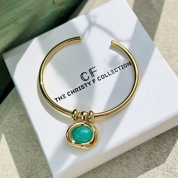 Gold bracelet with a green gemstone on a white box with 'The Christy F Collection' branding.