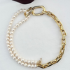 Gold chain and pearl necklace on a white surface with a dark leaf.