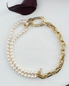 Gold chain and pearl necklace on a white surface with a dark leaf.