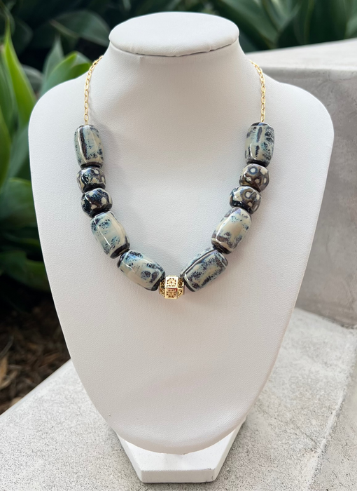 Necklace with blue beads on a white mannequin bust outdoors.