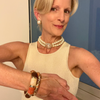 Woman wearing pearl necklace and bracelet, standing indoors with a neutral background