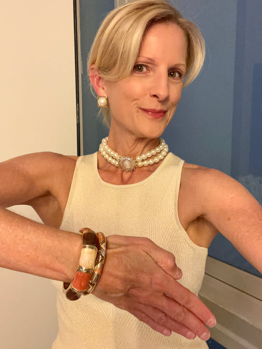Woman wearing pearl necklace and bracelet, standing indoors with a neutral background