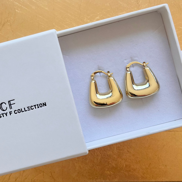 Gold hoop earrings in a Christy F Collection box on a wooden surface
