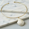 A delicate gold wire bangle necklace with a textured white shell pendant, displayed on a white marble background.
