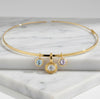 A gold necklace with three hanging charms, including a central round bezel-set clear stone and two smaller round stones, displayed on a white marble block.