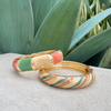 Gold bangle with multicolored stones on a textured surface with green leaves in the background