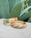 Gold bangle with multicolored stones on a textured surface with green leaves in the background