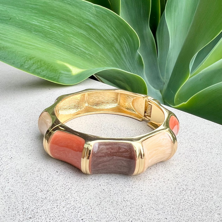 Gold bracelet with enamel accents on a textured surface with green leaves in the background