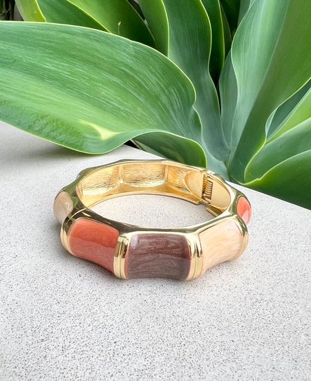 Gold bracelet with enamel accents on a textured surface with green leaves in the background