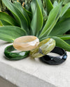 Set of four resin bangles on a stone surface with green leaves in the background
