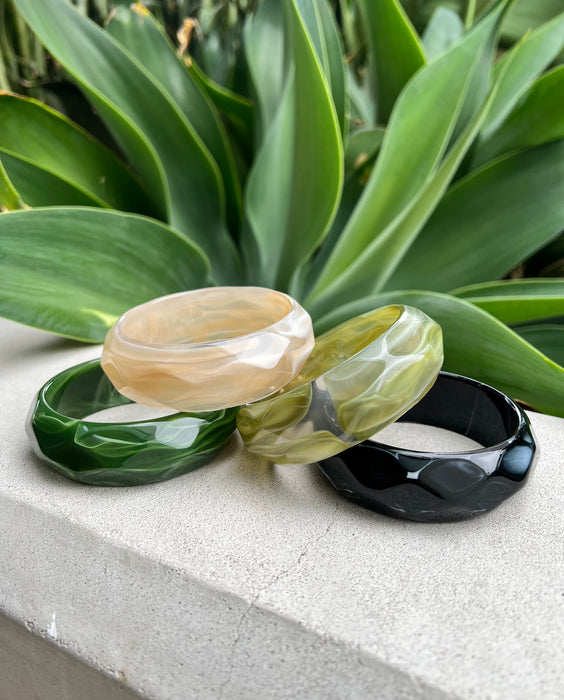 Set of four resin bangles on a stone surface with green leaves in the background