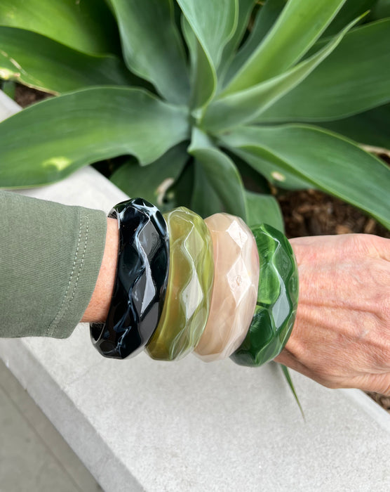 Person wearing multiple marbled patterned bracelets on a plant background
