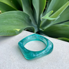 Teal bracelet on a textured surface with green leaves in the background