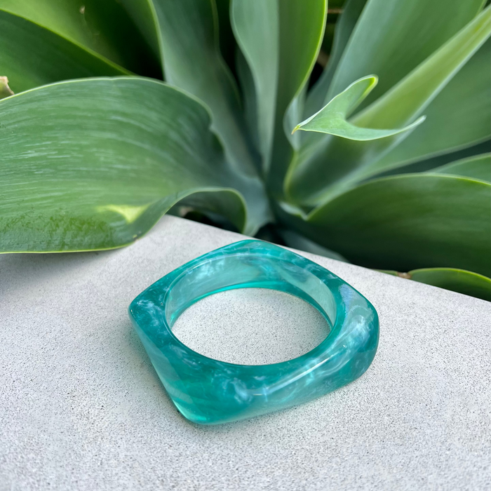 Teal bracelet on a textured surface with green leaves in the background