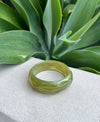 Green bracelet on a white surface with green leaves in the background