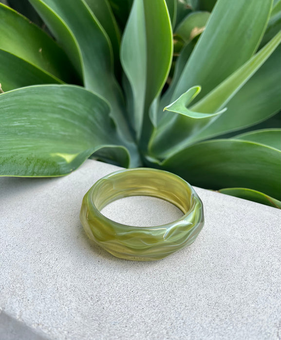 Green bracelet on a white surface with green leaves in the background