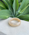 Beige bracelet on a white surface with green leaves in the background